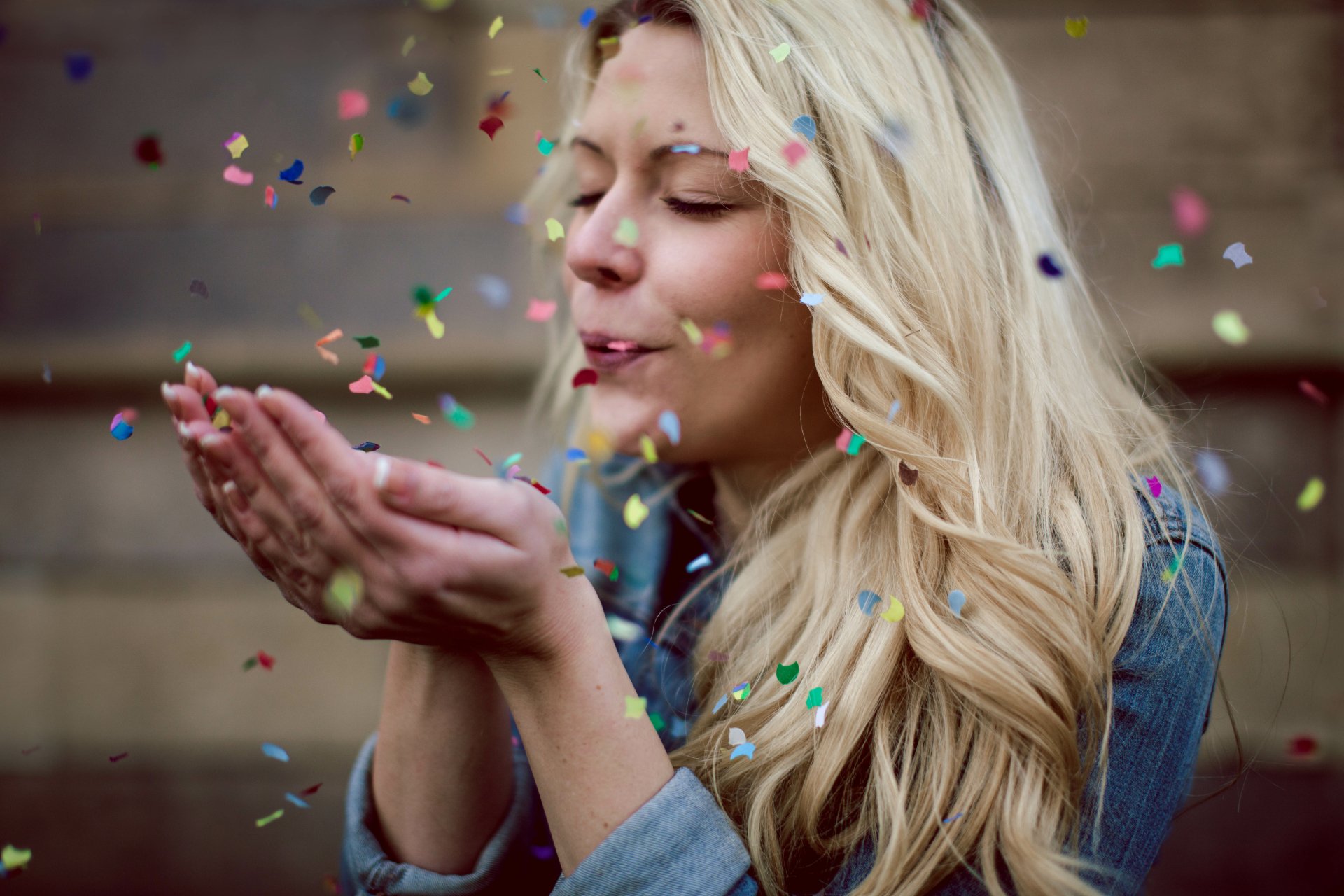 A blonde woman model blows colorful confetti amidst bokeh lights, captured in a vibrant 4K Ultra HD desktop wallpaper background.
