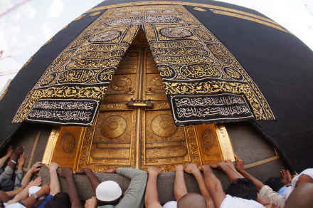 A close-up of the Kaaba's ornate entrance, showcasing its intricate golden doors and richly embroidered covering, surrounded by worshippers in a moment of reverence. HD desktop wallpaper.