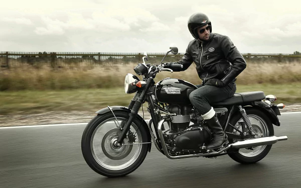 HD PC desktop wallpaper showing a rider on a classic Triumph Bonneville motorcycle cruising on an open road.