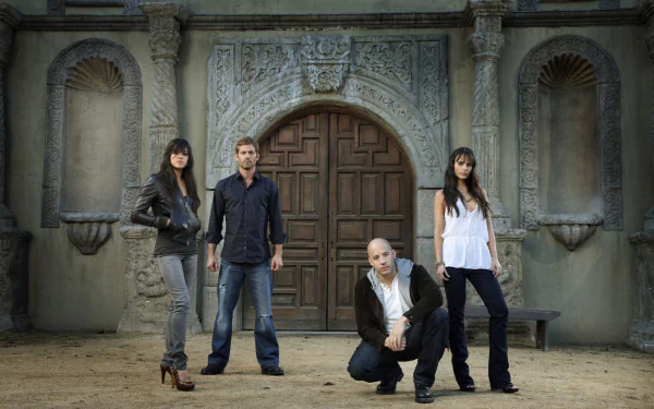 A dramatic scene featuring the main characters from Fast & Furious: Letty Ortiz, Brian O'Conner, Dominic Toretto, and Mia Toretto against a striking architectural backdrop.