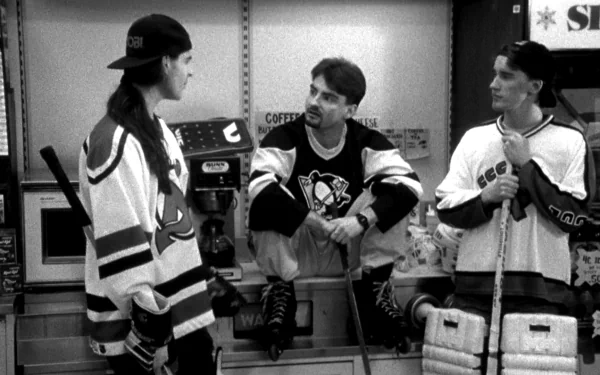 Black-and-white HD desktop wallpaper of three young men in hockey jerseys joking at a convenience-store counter — a scene from the movie Clerks.