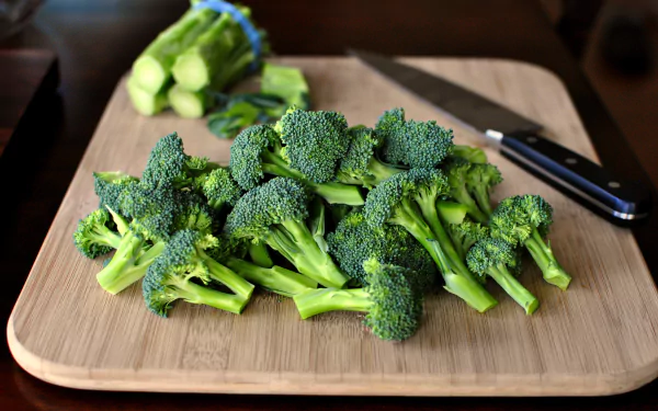 2K Quad HD PC desktop wallpaper of fresh broccoli florets on a wooden cutting board with a chef’s knife — food-themed background.