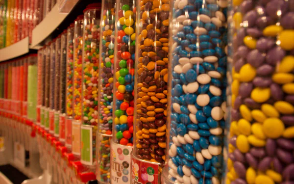 Colorful candy-coated chocolates fill transparent dispensers in a vibrant 4K Ultra HD desktop wallpaper, showcasing an enticing display of sweets.