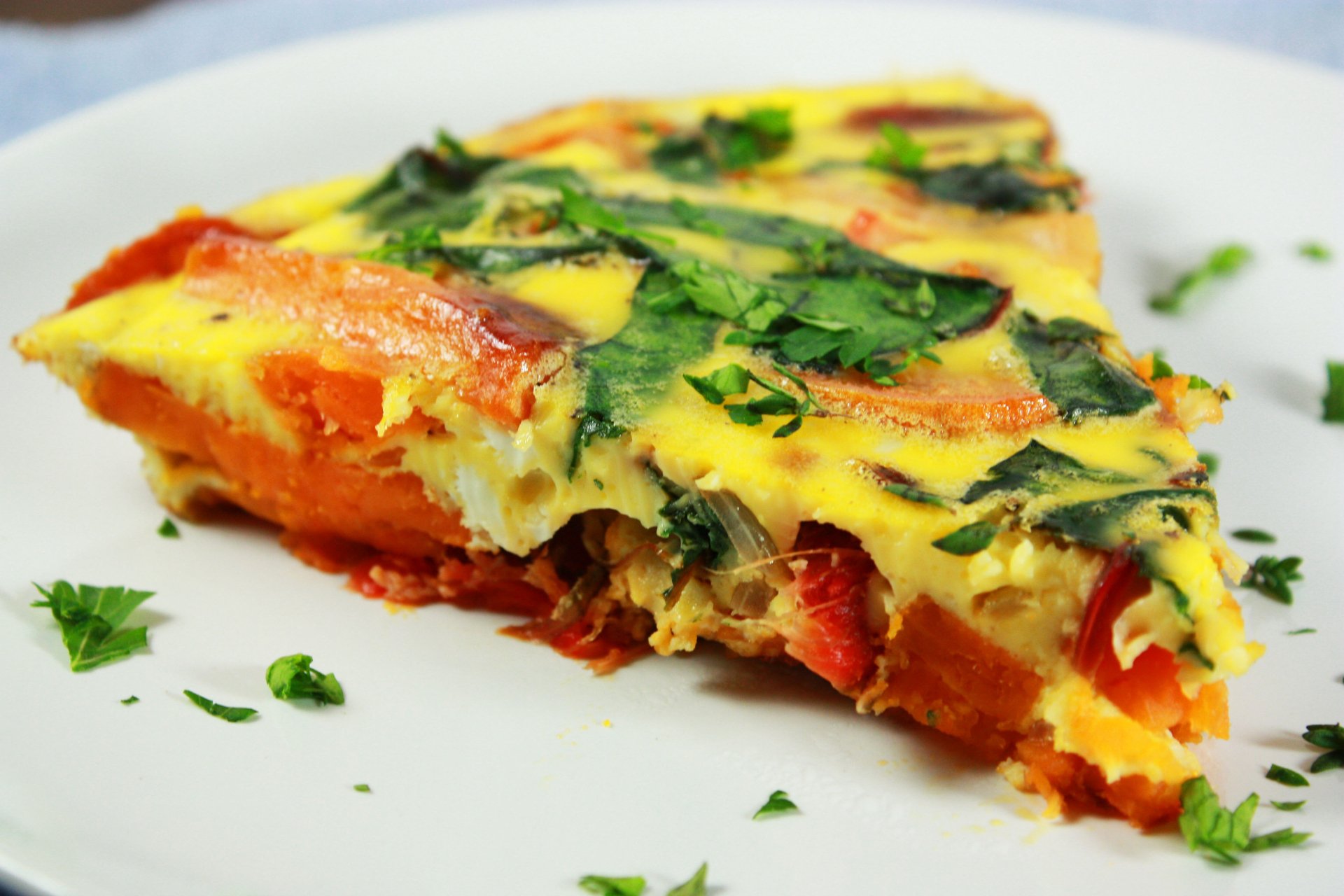 Close-up of a vibrant frittata slice with fresh herbs, tomatoes, and greens, captured in 4K Ultra HD as a PC desktop wallpaper featuring lunch and meal themes.