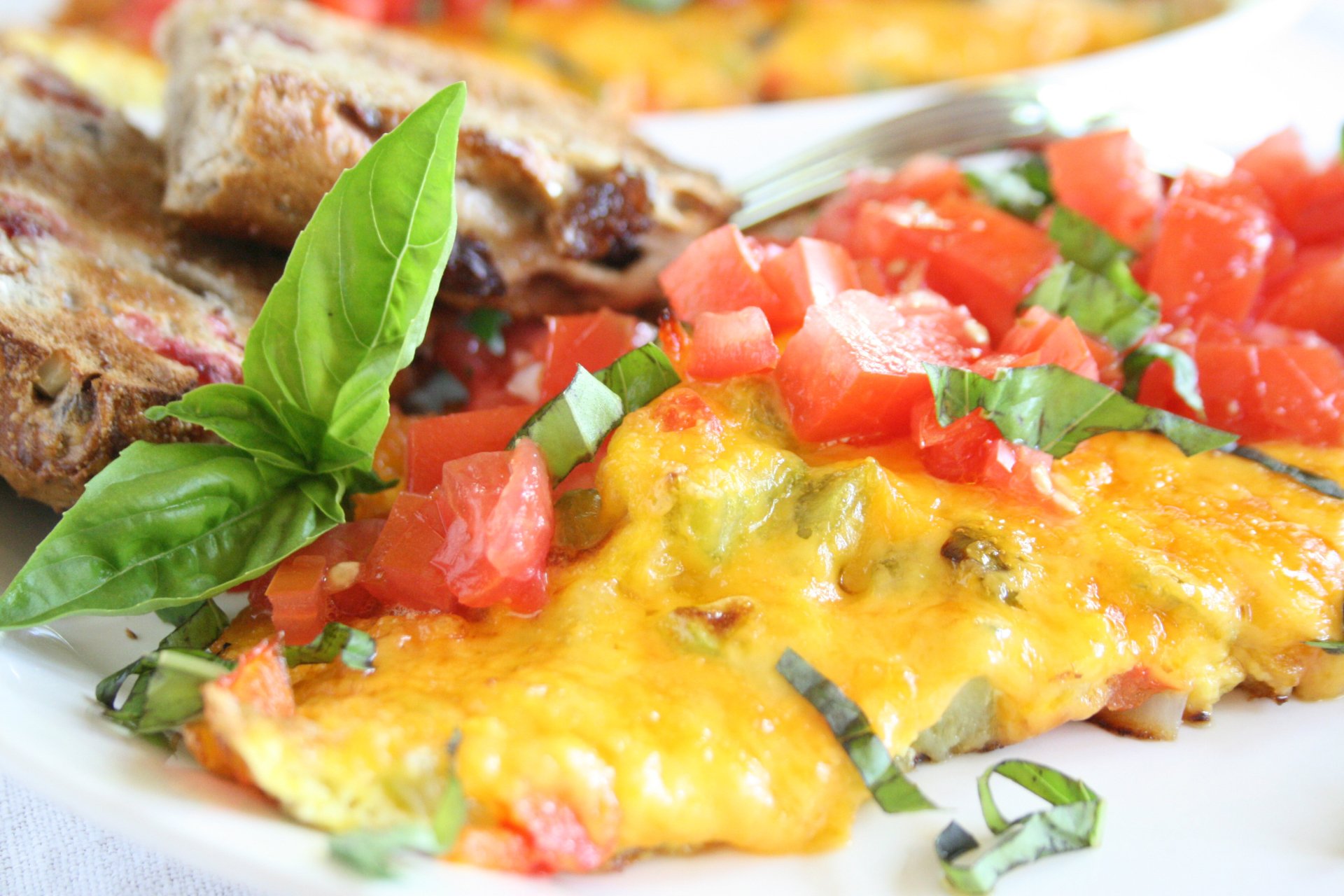 Close-up of a vibrant frittata topped with melted cheese, fresh diced tomatoes, and basil leaves, styled as an HD PC desktop wallpaper and background.