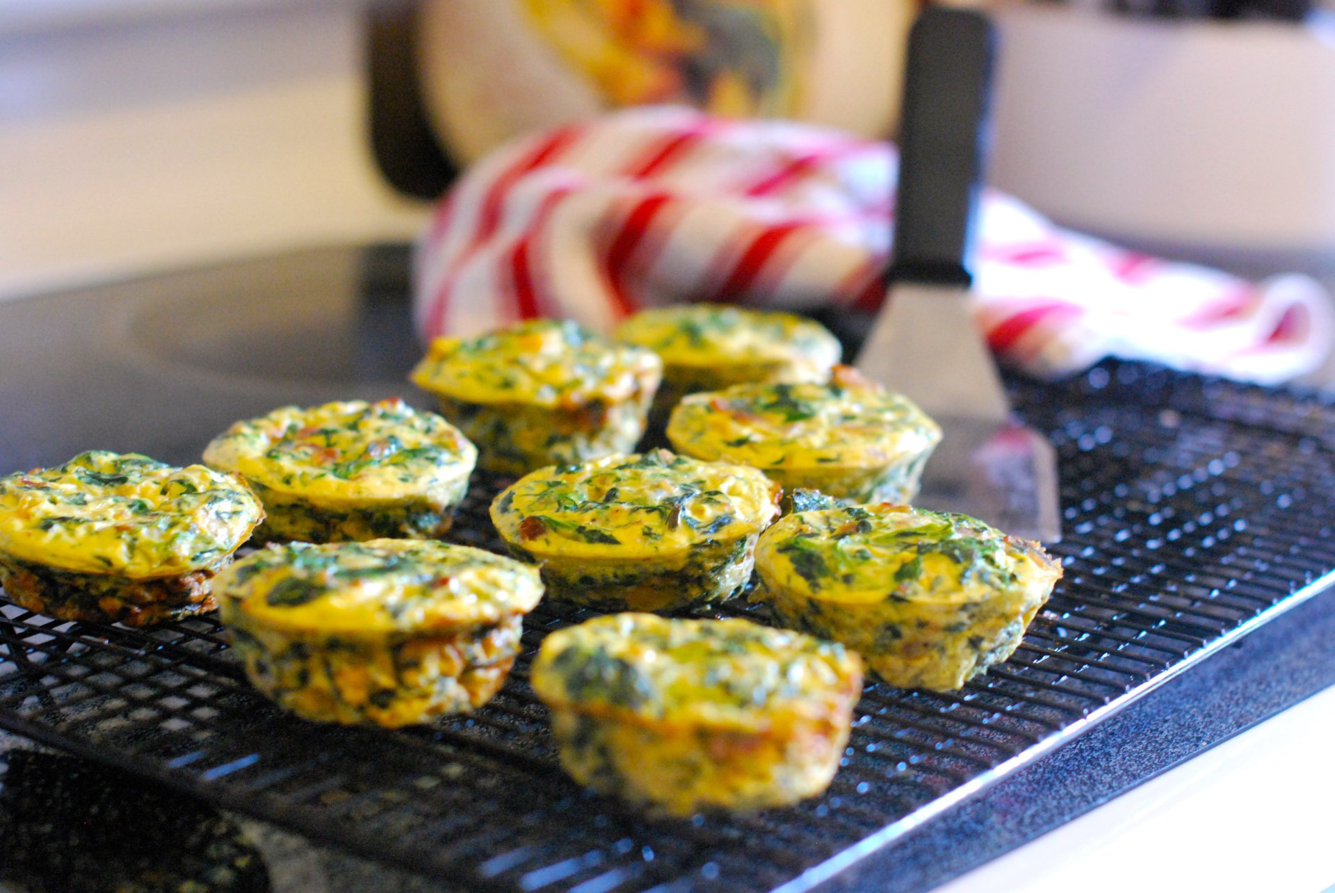 A close-up of mini spinach and cheese frittata muffins cooling on a wire rack, presented as a vibrant 4K Ultra HD desktop wallpaper with a cozy kitchen background.