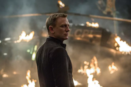 Daniel Craig as James Bond in an action scene from the movie Spectre, with flames and a helicopter in the background.