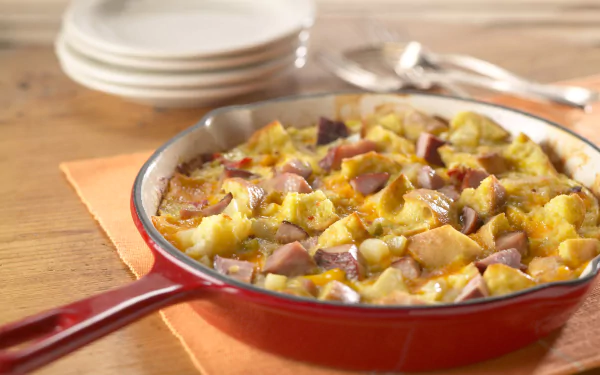 HD desktop wallpaper featuring a savory frittata meal with potatoes and sausage in a red skillet on a wooden table, ready to serve.