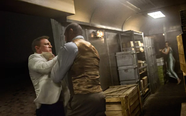 HD PC wallpaper of a tense Spectre movie scene: James Bond grabs an opponent in a dim cargo hold while Madeleine Swann watches from the background.