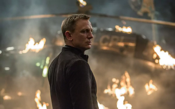 Daniel Craig as James Bond in an action scene from the movie Spectre, with flames and a helicopter in the background.
