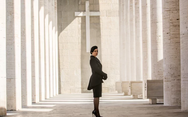 Monica Bellucci as Lucia Sciarra stands elegantly in a stunning architectural setting from the movie Spectre, featuring light streaming through tall columns and a cross in the background.