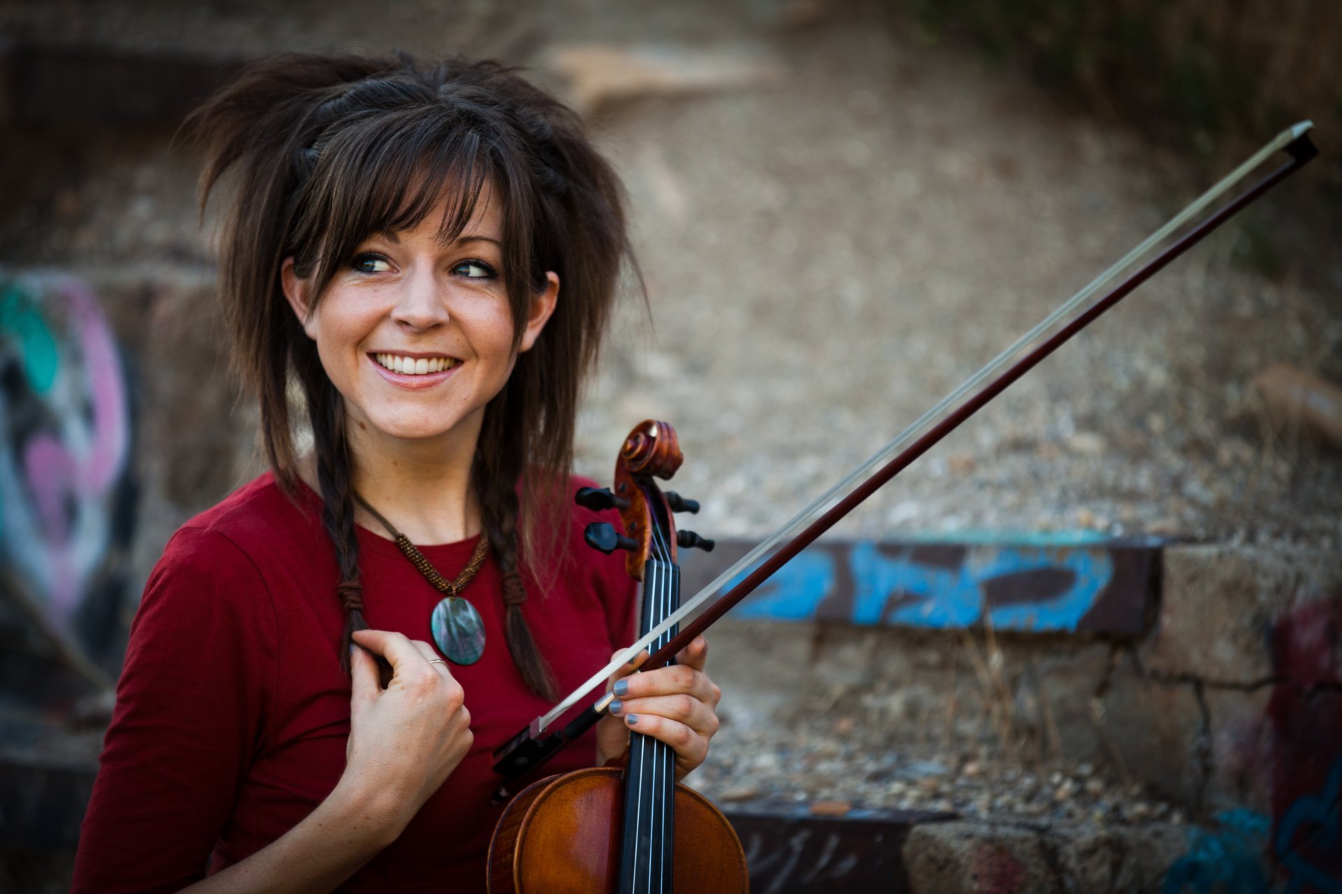 Lindsey Stirling smiling with her violin in hand against an urban backdrop, captured in vibrant 4K Ultra HD for a music-themed PC desktop wallpaper.