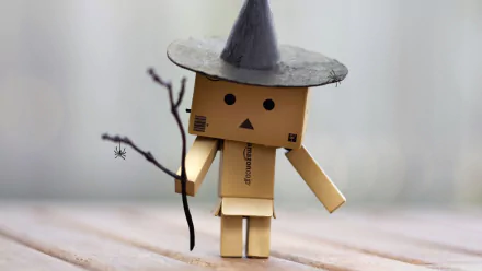 A Danbo figure wearing a pointed witch hat and holding a small branch with a spider, set against a soft, blurred background. HD PC desktop wallpaper.
