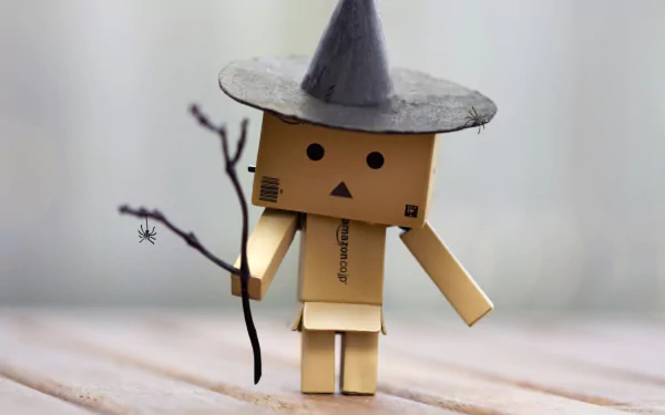 A Danbo figure wearing a pointed witch hat and holding a small branch with a spider, set against a soft, blurred background. HD PC desktop wallpaper.