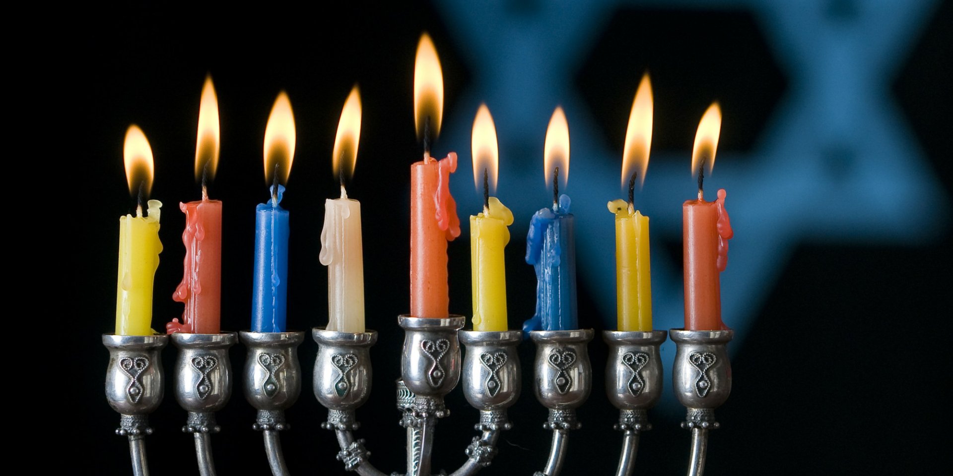 HD PC desktop wallpaper of a Hanukkah menorah with nine lit colorful candles against a dark blue background, capturing the holiday's festive spirit.