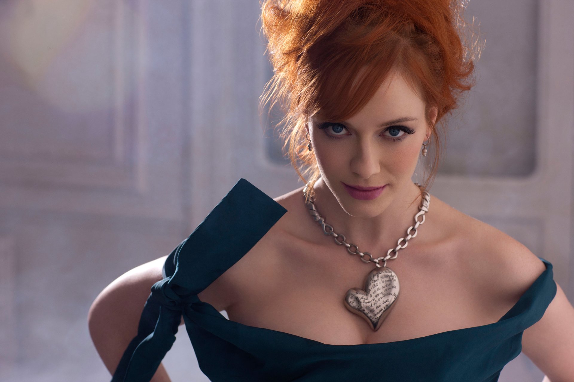 A high-definition wallpaper featuring American actress Christina Hendricks, showcasing her striking red hair and elegant attire, highlighted by a bold heart-shaped necklace.