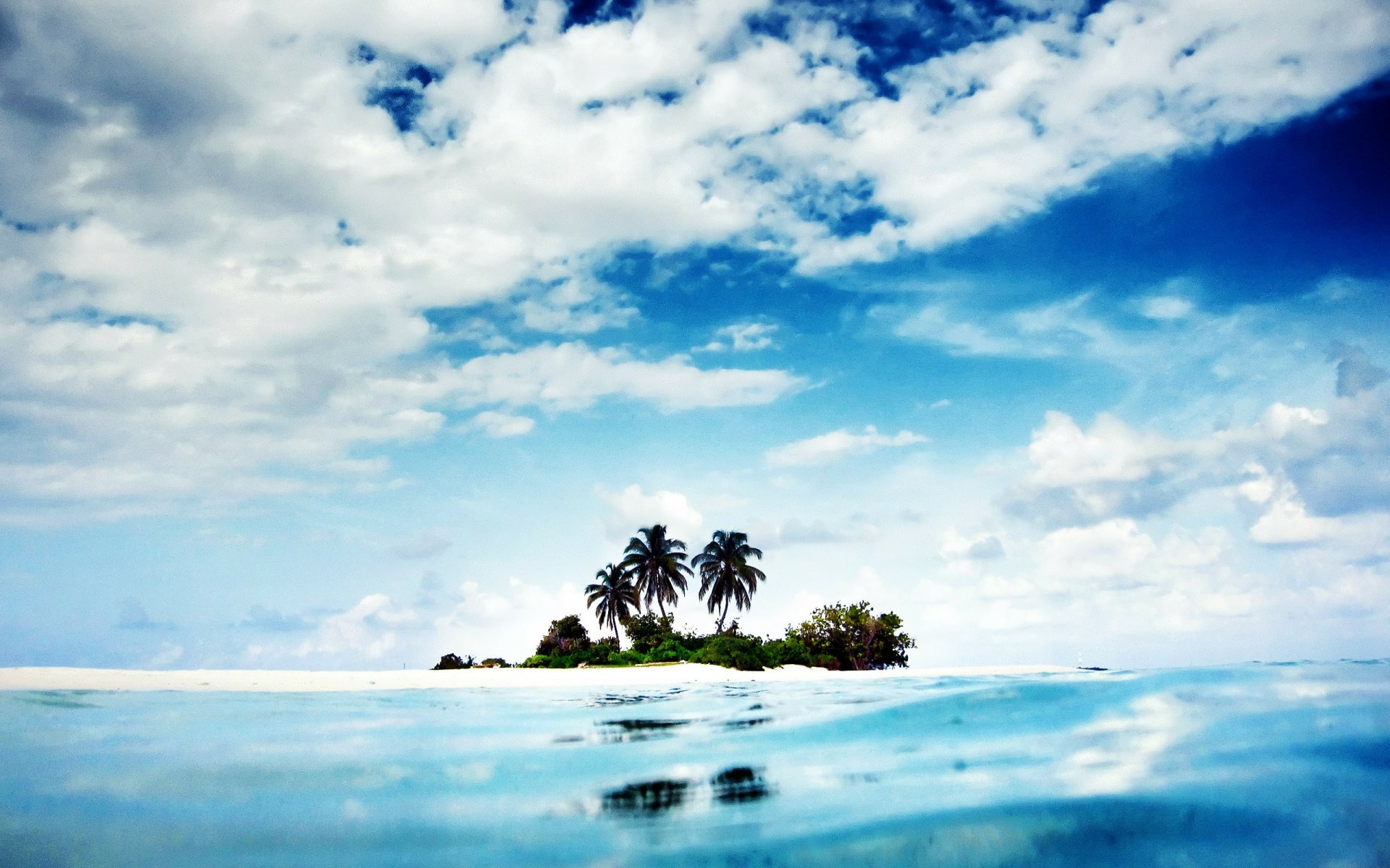 2K Quad HD PC desktop wallpaper: small tropical island with palm trees on white sand, turquoise water under a blue sky with scattered clouds — nature island background.