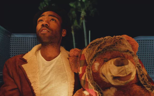 A HD PC desktop wallpaper featuring Childish Gambino with a large teddy bear, set against a dark background with subtle greenery, highlighting a music-themed atmosphere.