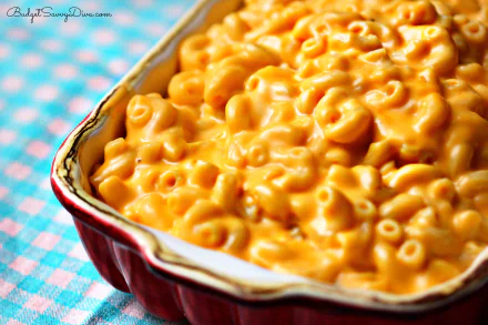 HD desktop wallpaper: close-up of creamy macaroni and cheese in a red baking dish on a blue-checkered cloth, golden pasta filling the frame.