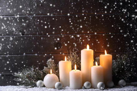 A serene image of glowing candles surrounded by soft snowflakes, set against a dark wooden backdrop, creating a warm and cozy atmosphere. Ideal as a HD desktop wallpaper or background.