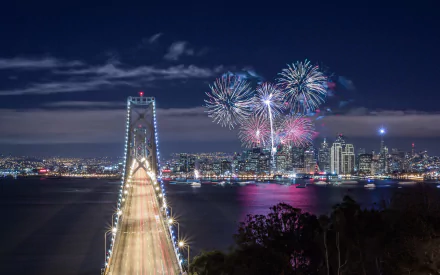 Night view of the Bay Bridge in San Francisco, California, illuminated with fireworks lighting up the city skyline in this HD desktop wallpaper.