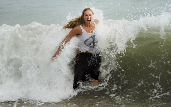 Ronda Rousey joyfully splashes through ocean waves, showcasing her vibrant spirit in this HD desktop wallpaper celebrating her dynamic presence in sports.
