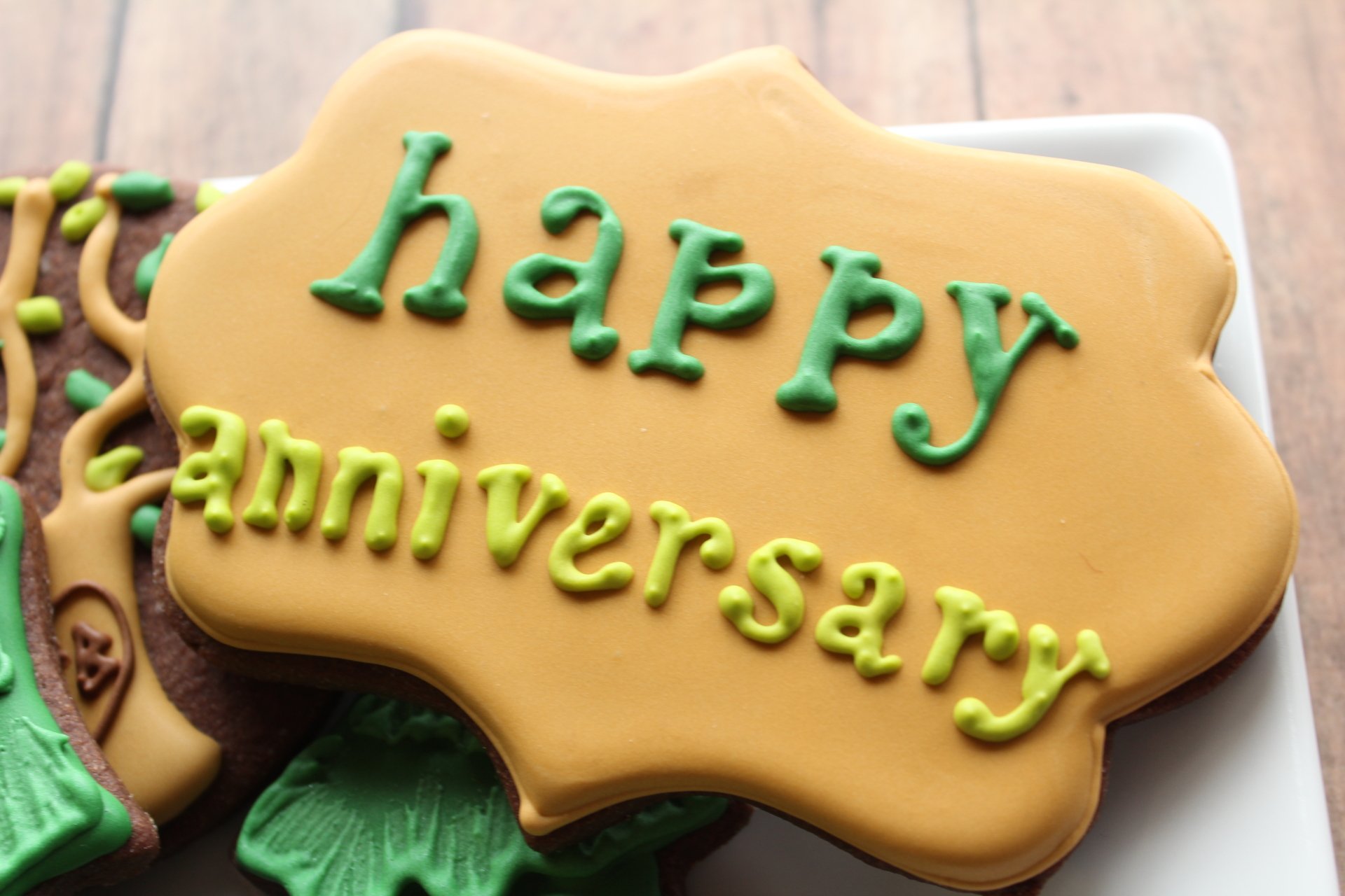 Holiday cookie iced happy anniversary in green on golden fondant, close-up; 5K Ultra HD PC desktop wallpaper/background.