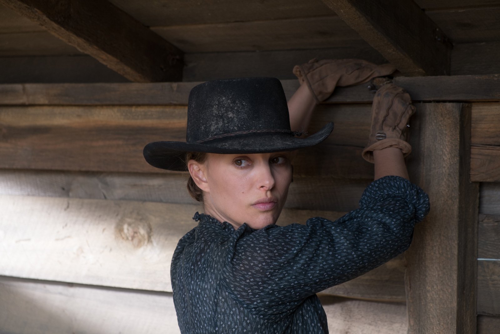 Woman in a cowboy hat and gloves leans against a wooden barn wall — still from the movie Jane Got a Gun; HD PC desktop wallpaper.
