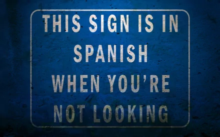 HD wallpaper with a humorous sign stating This sign is in Spanish when you're not looking on a blue background.