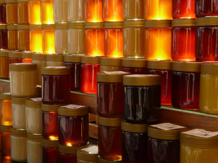 Rows of jars filled with various honey and sweet spreads, glowing warmly in rich amber and golden hues, displayed as a vibrant HD desktop wallpaper background.