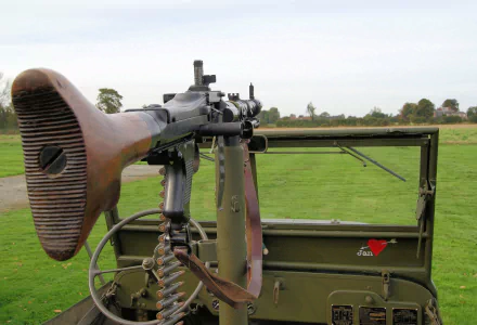 A detailed close-up of an MG-34 machine gun mounted on a vehicle, showcasing its wooden stock and ammunition belt, set against a grassy landscape, creating a striking HD desktop wallpaper.