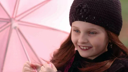 A young girl smiles while holding a pink umbrella, wearing a stylish black hat. This image features Abigail Breslin from the movie The Ultimate Gift, serving as a vibrant HD wallpaper.