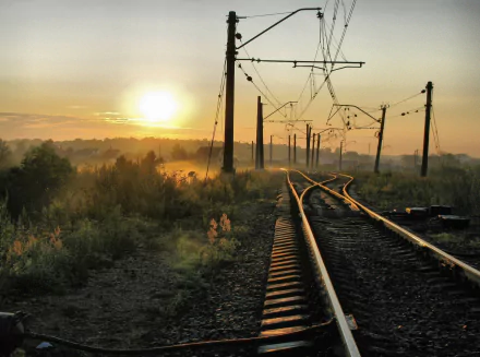 A serene HD wallpaper featuring a winding railroad track under a warm sunrise, framed by tall grasses and electric poles, capturing the essence of man-made beauty in nature.