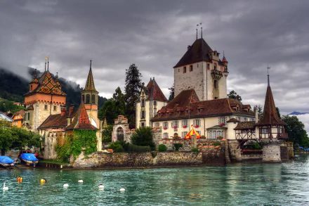 Oberhofen Castle in Switzerland stands majestically by the water under a dramatic cloudy sky, showcasing its historic man-made architecture in vivid detail.