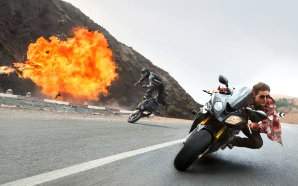 Action-packed HD wallpaper from *Mission: Impossible - Rogue Nation*, featuring intense motorcycle pursuit and a dramatic explosion in a breathtaking landscape.