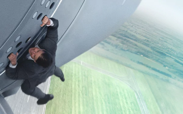 A high-definition desktop wallpaper from Mission: Impossible - Rogue Nation, featuring a character courageously clinging to the side of an aircraft against a dramatic backdrop.