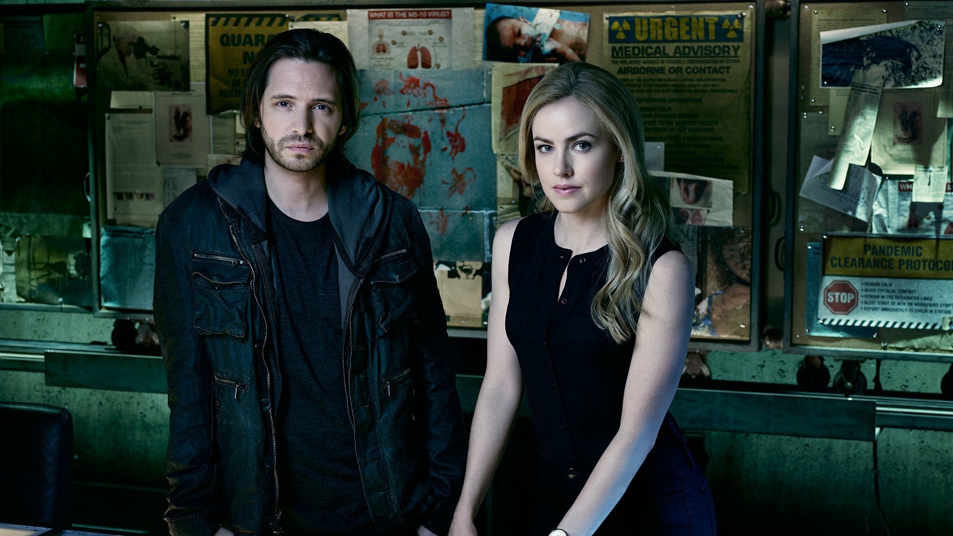 HD PC desktop wallpaper: promotional image from the TV show 12 Monkeys — two characters stand in a dim, cluttered investigation room with a bulletin board background.