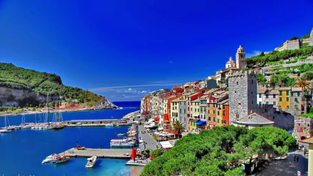 Scenic HD wallpaper of Porto Venere, Italy featuring a vibrant coastal town, boats docked in the harbor, and clear blue skies along the picturesque coastline.