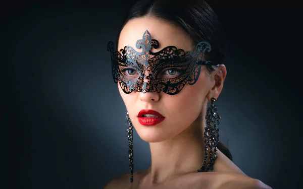 A brunette woman with striking green eyes and bold red lipstick gazes intently, wearing a decorative black mask and elegant earrings, creating an intriguing photographic portrait.