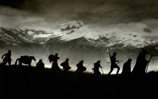 Silhouetted Fellowship of the Ring members trekking across a misty landscape with snow-capped mountains in the background, HD desktop wallpaper from The Lord of the Rings movie.