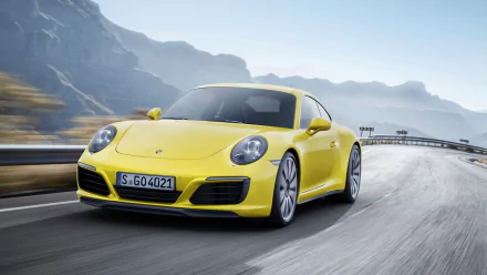 A vibrant yellow Porsche 911 Carrera accelerates along a winding road, surrounded by mountainous scenery, showcasing the vehicle's sleek design and dynamic presence.