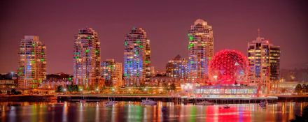 A vibrant night cityscape of Vancouver, showcasing illuminated high-rise buildings and the iconic red dome, reflecting beautifully on the water.