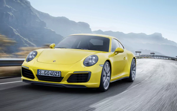 A vibrant yellow Porsche 911 Carrera accelerates along a winding road, surrounded by mountainous scenery, showcasing the vehicle's sleek design and dynamic presence.