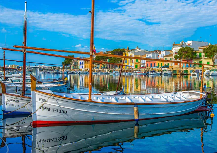 Colorful boats docked in a man-made harbor along the vibrant coast of Majorca, Spain, under a bright blue sky in this HD desktop wallpaper.