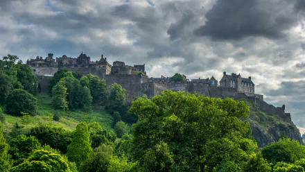 2K Quad HD PC desktop wallpaper: Edinburgh Castle perched on a rocky crag under brooding clouds, verdant trees framing the man-made fortress.