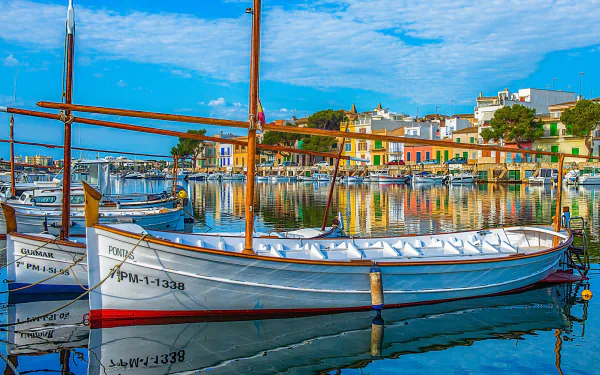 Colorful boats docked in a man-made harbor along the vibrant coast of Majorca, Spain, under a bright blue sky in this HD desktop wallpaper.