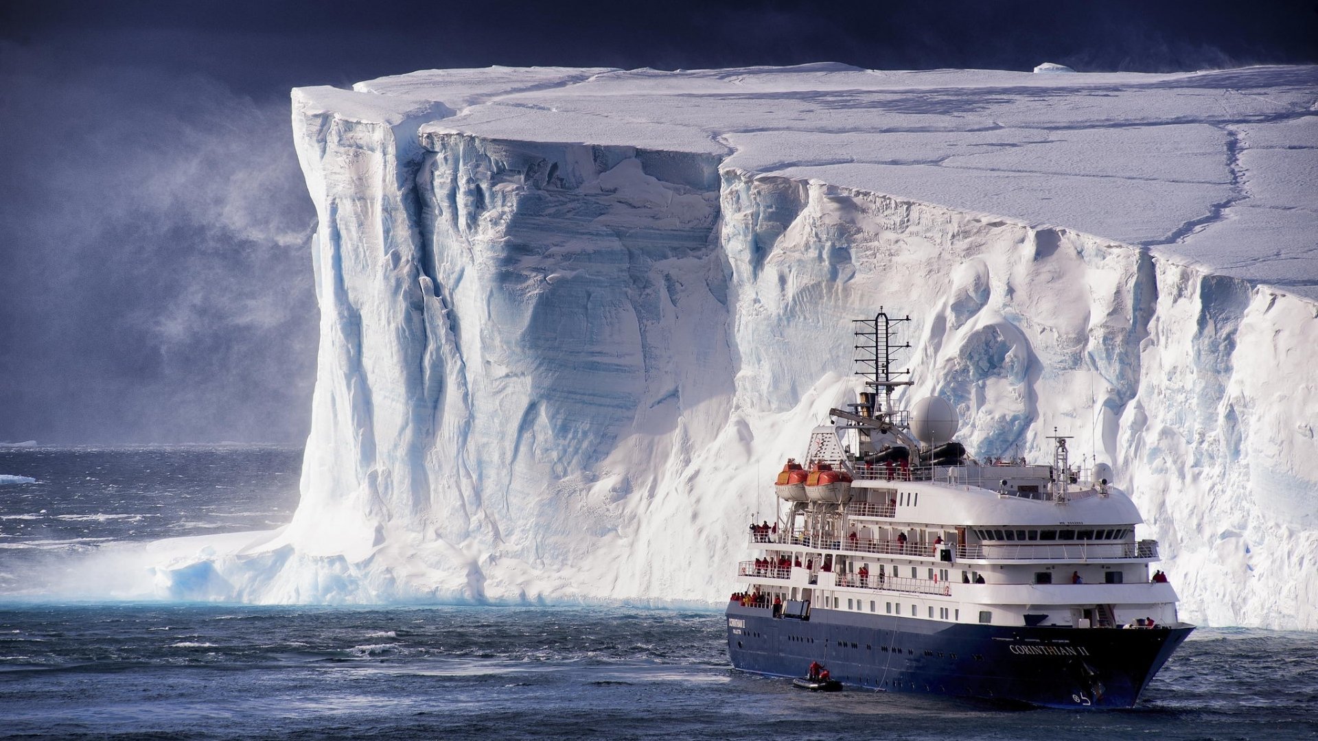 HD desktop wallpaper showing a cruise ship navigating icy waters near towering glacier cliffs under a cloudy sky.
