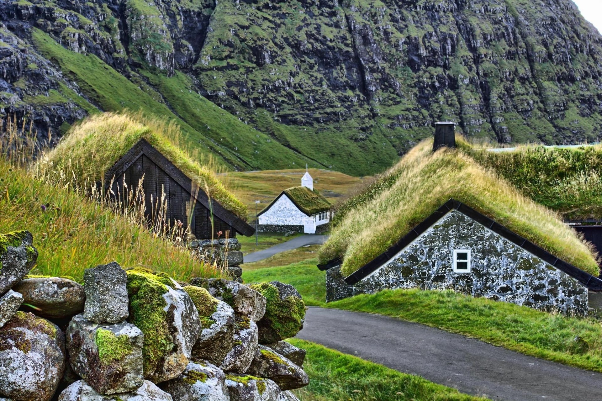 HD PC desktop wallpaper and background: man-made village of grassy-roofed stone houses tucked in a green valley beneath rugged cliffs.