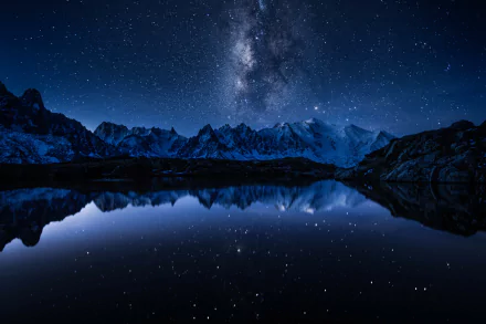HD desktop wallpaper of a night landscape featuring the Milky Way over mountains. The night sky and stars reflect in a tranquil body of water.