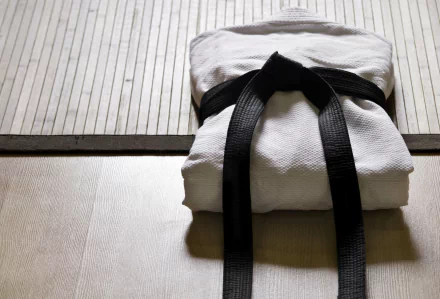 HD desktop wallpaper featuring a neatly folded white judo gi with a black belt resting on a wooden floor, highlighting the sport's discipline and tradition.